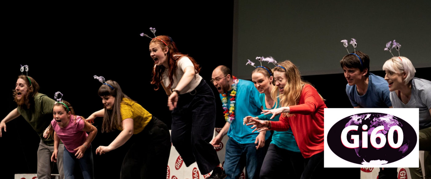 9 Actors leaping forwards towards the audience from Gi60 branded blocks whilst wearing strange deely-boppers. The Gi60 global logo is in the bottom right corner.