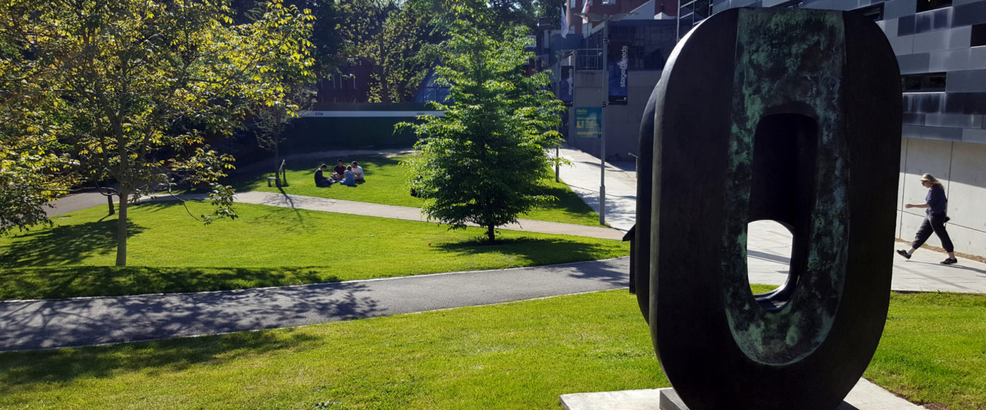 The Barbara Hepworth sculpture Dual Form situated outside stage@leeds. Dual Form is one of an edition of seven bronzes, a medium that Hepworth began working in towards the late 1950s. The sculpture is in front of the green space outside stage@leeds which includes two trees.