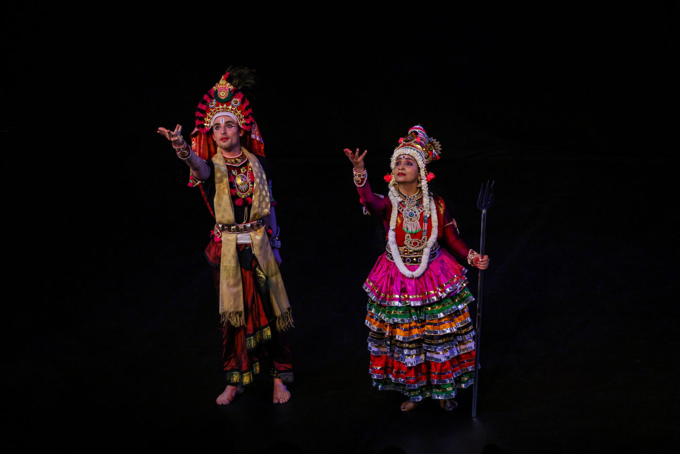 Devika and her dance partner in traditional Indian dress dancing with right arms outstretched.