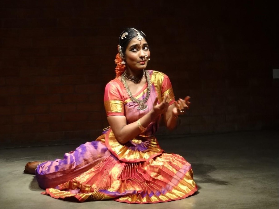 A Soth Asian dancer is a brighly coloured costumecan be seen kneeling on stage